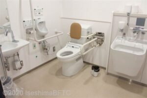 1階車いす対応トイレ内部　入口から見て左奥に、たて置きに便器がある。入口からみて左手前に洗面台