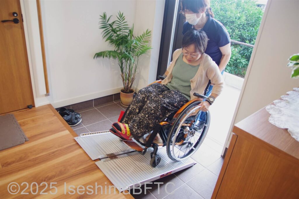 同行者のサポートでスロープを使って玄関から中にあがる車いす利用者