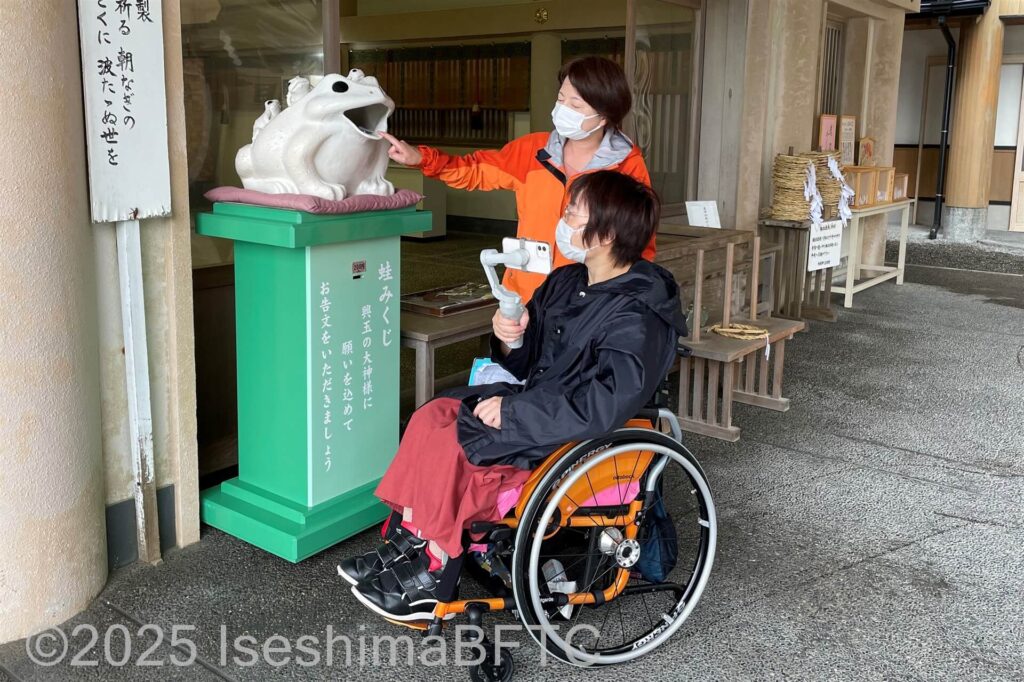 蛙みくじを引く車いす利用者と同行者