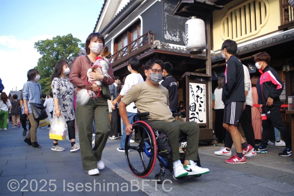 おはらい町を通行する車いす利用者と愛犬を抱えて歩く同行者