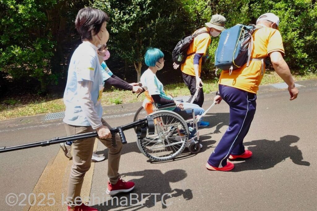 坂道でボランティアのサポートを受ける車いす使用者