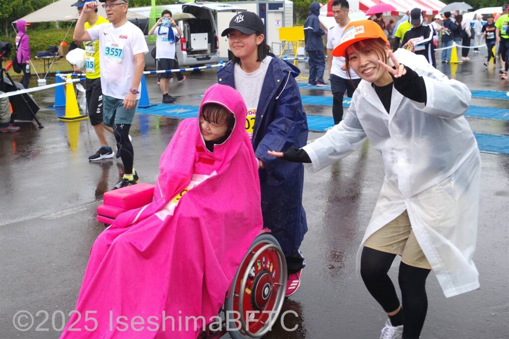 車いすの参加者とピースで笑顔のボランティアスタッフ
