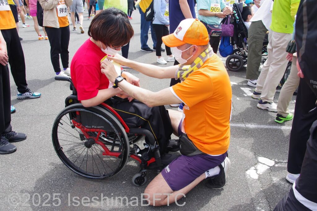 車いす選手にゼッケンをつけるボランティア