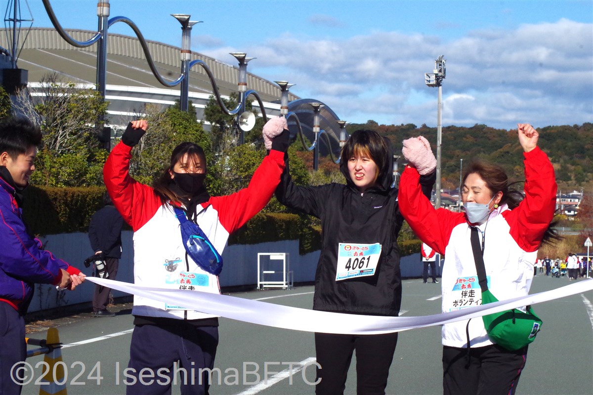 二人の伴走ボランティアと両手をつないでゴールテープを切る選手