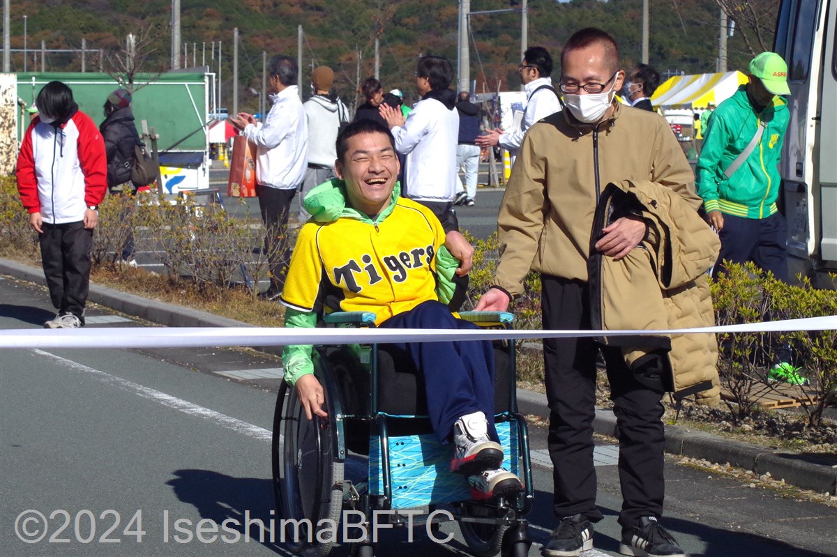 車いすを押してもらってゴールテープを切る選手