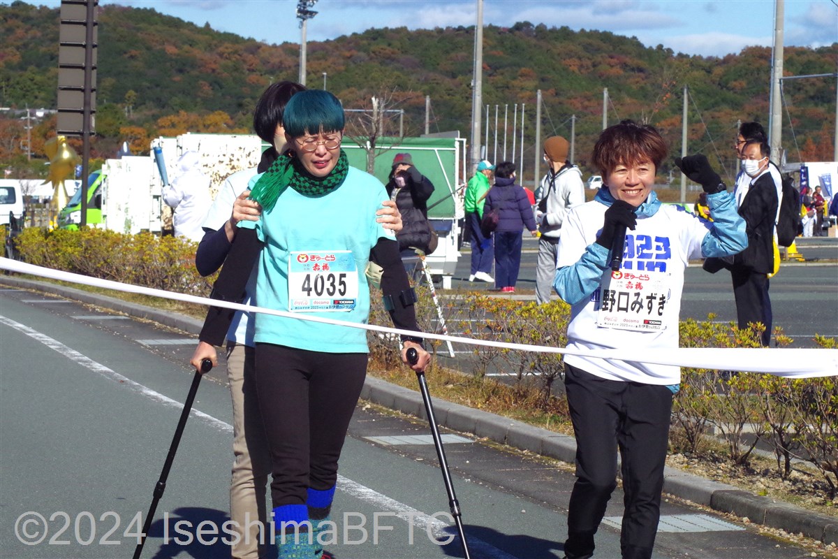 杖歩行でゴールテープを切る選手 隣で野口みずきさんが激励している