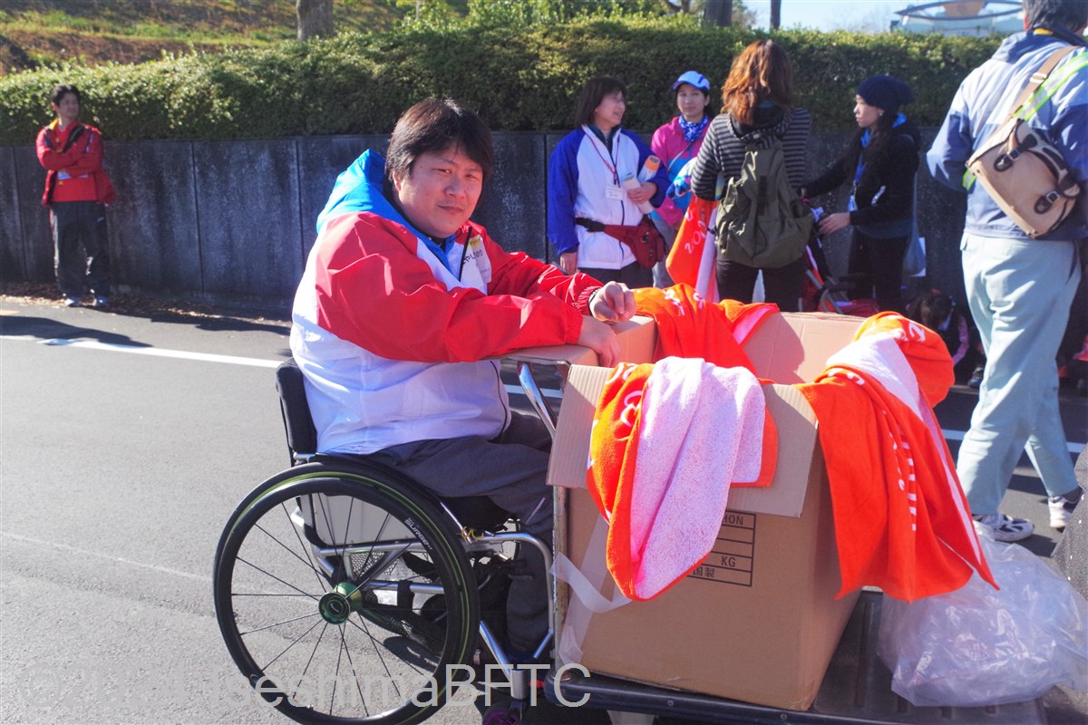 ゴールした選手にバスタオルを渡す準備をしている車いすのボランティア