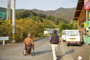 みかん畑に向かうっ車いすの男性とスタッフの後ろ姿。