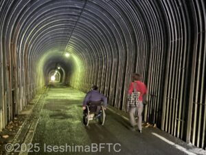 トンネルを歩いている男女。男性は車いすに乗っている。