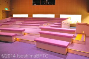 映像展示室のようす。座面が薄紫色のベンチが段々になっている客席に配置されている。車いすの方は最前列の段差がないところで視聴できる。