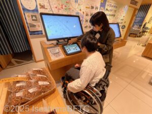 スタッフの説明を受けながら、モニターに映し出される地図を基に、オリジナルの地図を作製している車いすの女性。