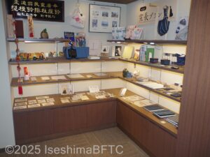 ショップコーナーのようす。棚の上には陶器の鈴、ポストカード、松坂木綿の手帳などが並んでいる。