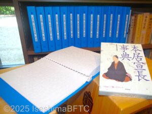 点字の本を開いたようす。その後ろには本居宣長辞典を点訳した本が15冊ほど並んでいる。