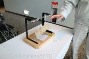 1階のホールにあるテーブルの上に置かれた触れる展示物。
両脇を紐でくくって吊り下げられているさ細長い鉱石とその脇に置かれている小さなハンマー。鉱石の名前はサヌカイトといい、 叩くと澄んだ音がする。