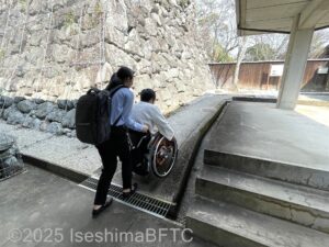 記念館を出た正面にある、旧宅へと続く坂道を上る女性2名。一人は車いすに乗っていて、もう一人の女性が介助している。