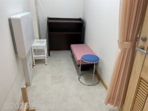 授乳室の室内のようす。細長い部屋に、ピンクの小さめの長椅子と青い丸いす、壁には折りたたみ式のベビーシートが設置されている。