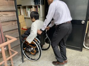 スロープを上がった先の扉から車いすの女性が男性の介助で建物の中に入っているようす。