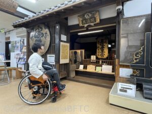 資料館1階のようす。昔の商店を模した展示を眺めている車いすの女性のようす。