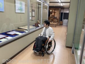 ガラスケースに展示されている資料を眺める車いすの女性のようす。