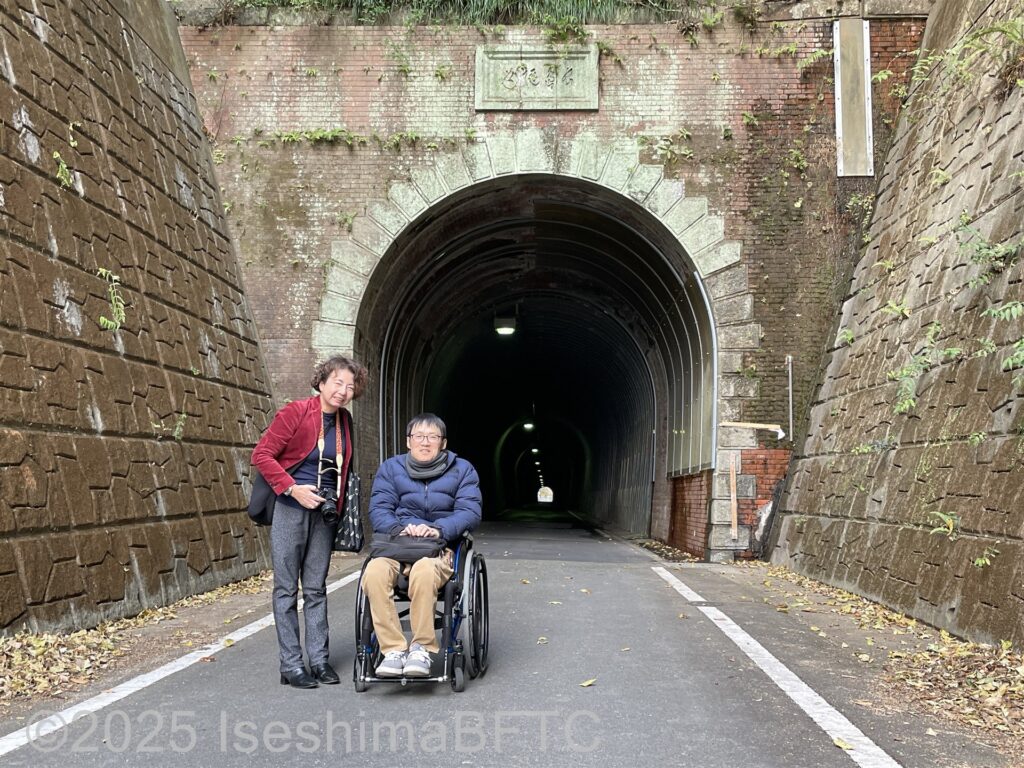 トンネルの前でこちらを向く男女。男性は車いすの青年。