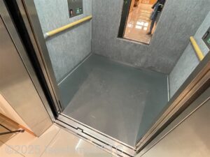 エレベーターの個室内がわかる写真。向かって左側には手すりが付いていて、奥には後方確認用の鏡も付いている。