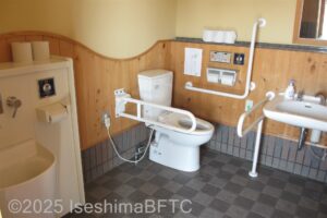 車いす対応トイレの個室内のようす。便器に向かって右側の壁にL字手すり、左側にU字の可動式手すりが付いている。