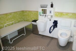 多目的トイレの室内のようす。便器に向かって右側の壁にはL字手すり、左側にはU字の可動式手すりあり。そのほかオストメイトやユニバーサルシートの設備もある。