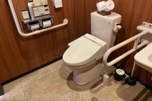 レストラン内にある車いす対応トイレの室内のようす。便器に向かって左側の壁にはL字手すりが付いていて、右側にはU字の可動式手すりが付いている。