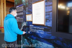 男性が会場内の展示パネルについている専用マークにタッチペンを近づけて、音声を流しているようす。