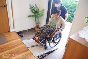 スロープを使って室内へ入る車いすの女性と、後ろからサポートする女性