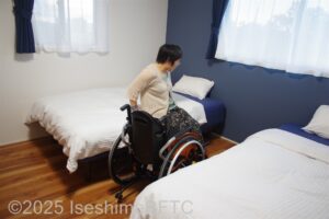 洋室2のベッドへ腰かけようとする車いすの女性