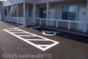 建物の横にある車いす対応駐車場　左側に車線が引かれ十分な広さあり　屋根はない
