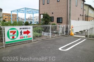 駐車場からコンビニに行く経路　セブンイレブンの看板があり、駐車場の柵が切れて、コンビニの駐車場に続く