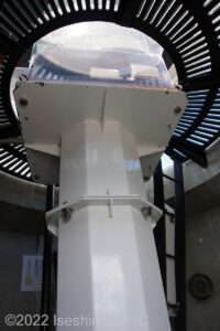白い鉄製の支柱の上に置かれている灯器を見上げているようす。