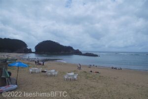 浜を見下ろしたようす。砂浜には白いイスとテーブルや青いパラソルも見える。