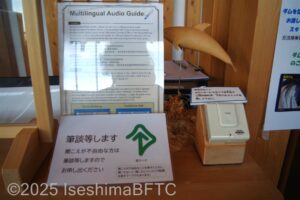 展示棟のカウンターに表示されている耳マークと音声ガイダンスの案内のようす。耳マークには「筆談いたします」の文字が書かれている。