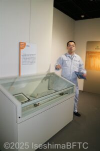 ガラスケースに展示されている鉱物について、説明をしている係員の姿。