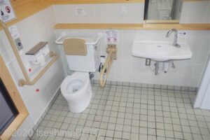 車いす対応トイレの個室内のようす。左壁にはL字手すり、右側にはU字の可動式手すりあり。便器の後ろ側には背もたれがついている。