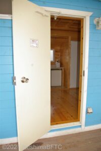 キャビンの玄関ドア。外壁は水色でドアは白色をしている。