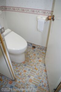 共用トイレ内の洋式トイレのようす。床にはカラフルなタイルが敷かれている。