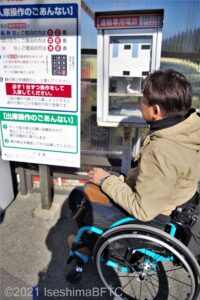 駐車場のゲート付近に設置されているボックスの中に入った電話で連絡をしている車いすの男性のようす。