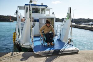 船のスロープから渡鹿野島の桟橋に上陸する車いすの男性のうようす。