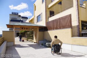 福寿荘の入口の門に向かって車いすの男性が進んでいるようす。