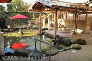 庭園露天風呂のようす。岩風呂と、木製の円形浴槽がある。周りは日本庭園のようなつくりで、赤いのだて傘が見える。