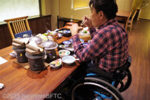 食事処のテーブルについて、食事をしている車いすの男性のようす。