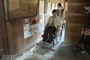 車いすの女性が入口の木戸から室内の土間へ入るようす