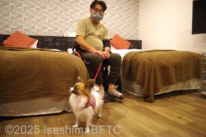 ベッドとベッドの間にいる車いすの男性と愛犬