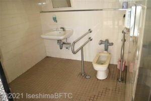 車いす対応トイレの個室内のようす。便器の左右にU字手すりが付いている。便器はバリアフリー型と呼ばれる小判型で、設備はかなり古い。