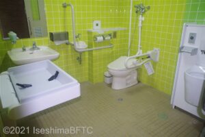 トイレ室内　入り口入って右壁にオストメイト　奥に便器壁面にはL字手すり　左壁に子ども用オムツ交換シート　その奥に洗面　水栓方法は上下のレバー