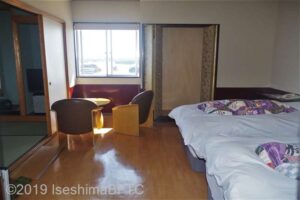 客室内のようす。洋室と8畳の和室がある。写真や洋室にシングルベッドが2台置かれているようす。窓際にはイス2脚とテーブルが置かている。